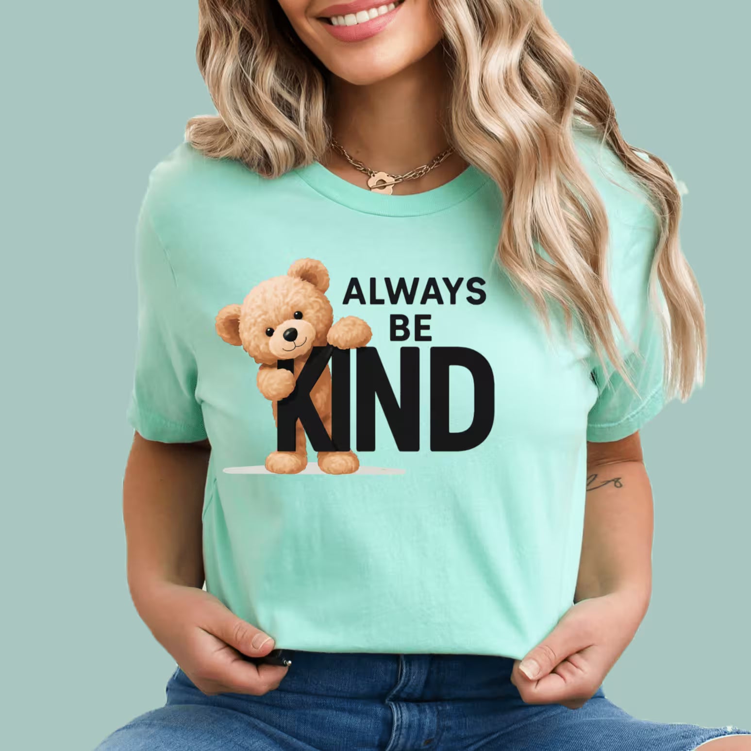Person wearing a Mint t-shirt with a teddy bear and 'Always Be Kind' text on a solid background