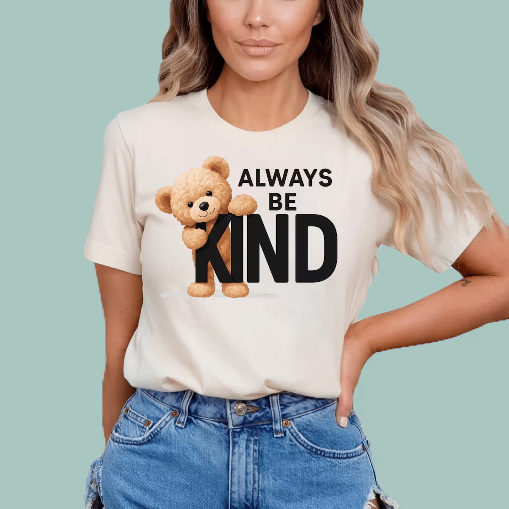 Person wearing a Natural t-shirt with a teddy bear and 'Always Be Kind' text on a light blue background
