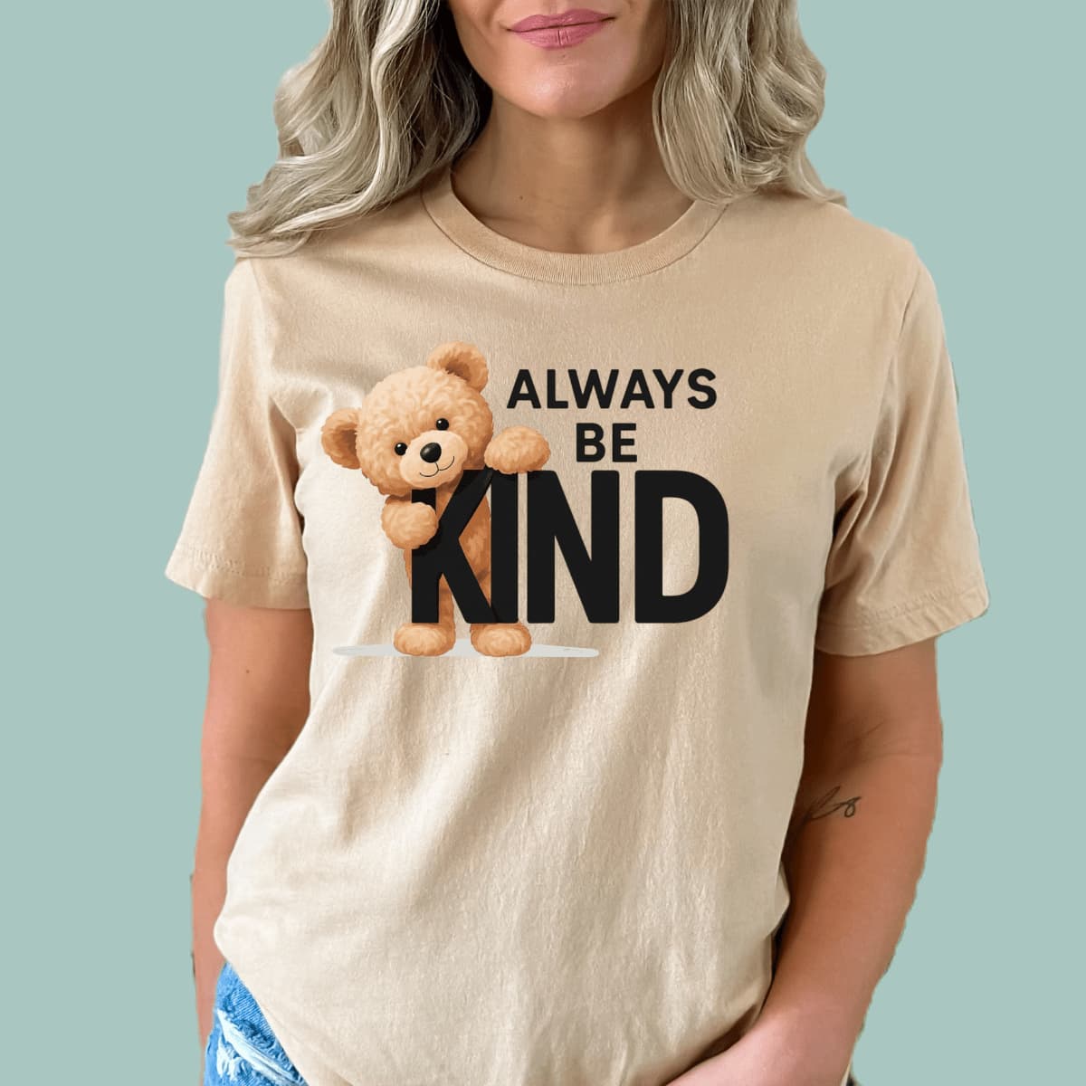 Sand t-shirt with a teddy bear and 'Always Be Kind' text on a light blue background
