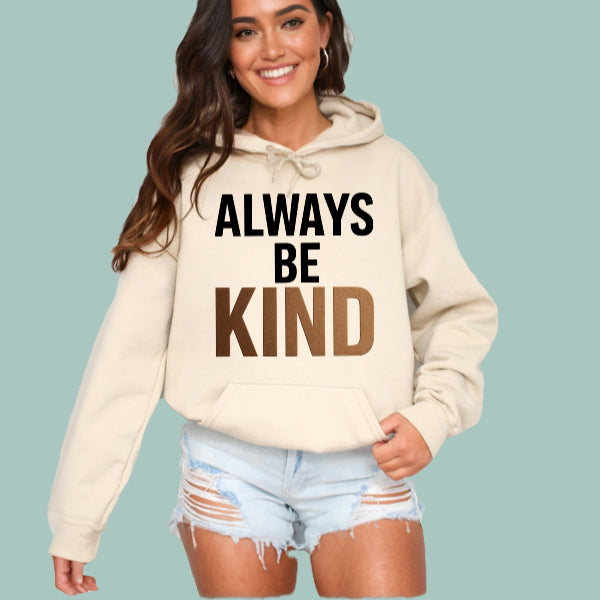 Woman wearing a beige hoodie with 'ALWAYS BE KIND' text on a light blue background
