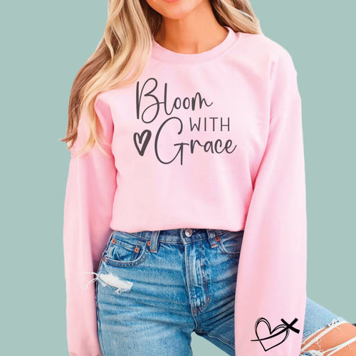 Woman wearing a pink "Bloom With Grace" Christian sweatshirt with a floral heart and script design.