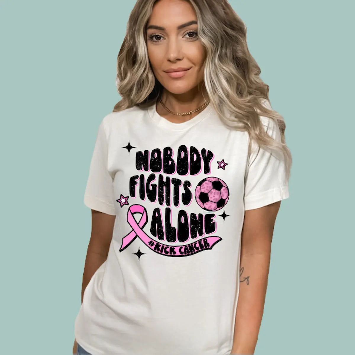 Woman wearing a Natural color 'No Body Fights Alone' t-shirt with a large pink ribbon graphic.
