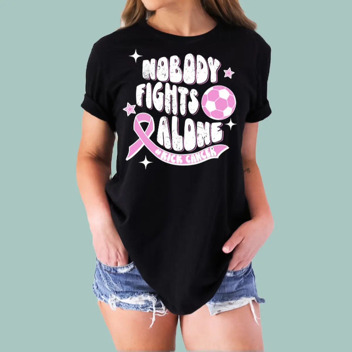 Woman wearing a black 'No Body Fights Alone' t-shirt with a large pink color ribbon graphic.