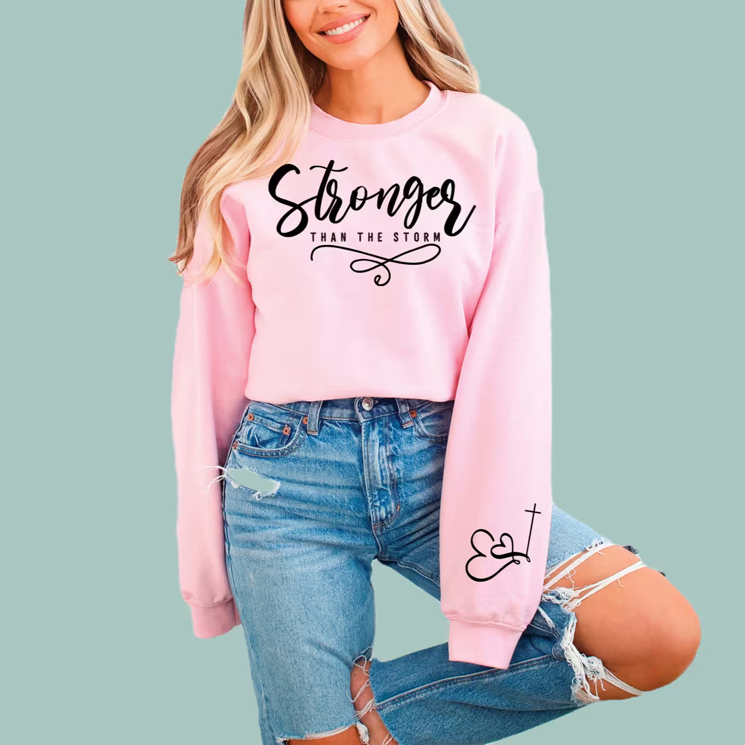 Pink inspirational faith sweatshirt featuring the "Stronger Than The Storm" resilience message.