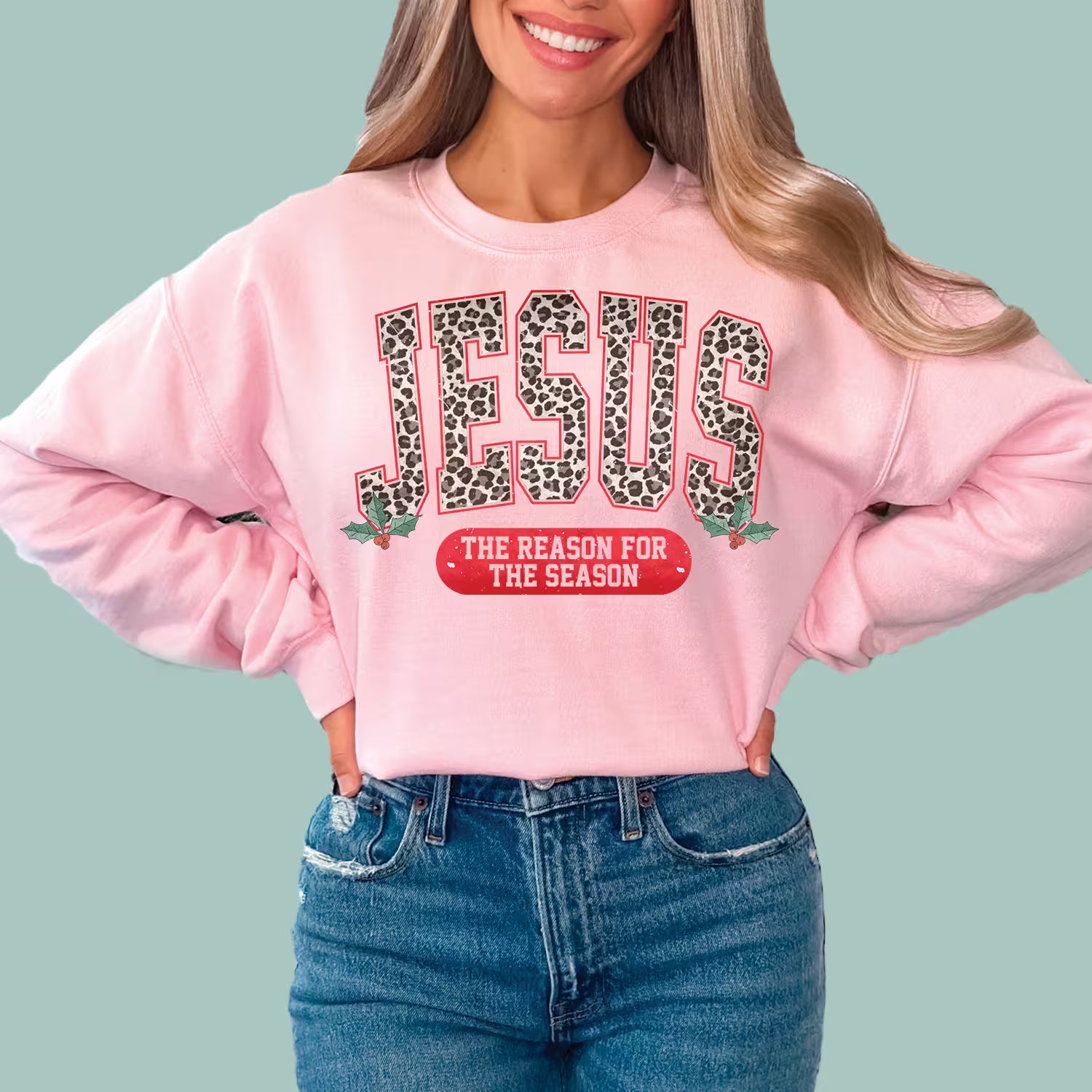 Woman wearing pink "Jesus The Reason For The Season" Christmas sweatshirt with leopard print text.