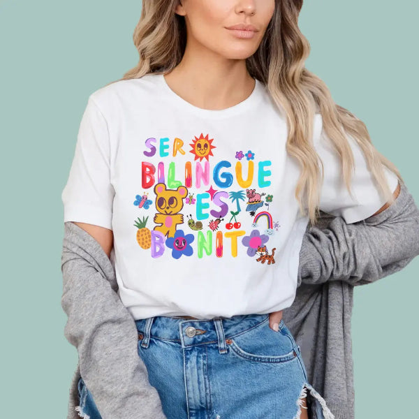 Person wearing a white sweatshirt with colorful text ser bilingual es bonito and graphics on a light blue background