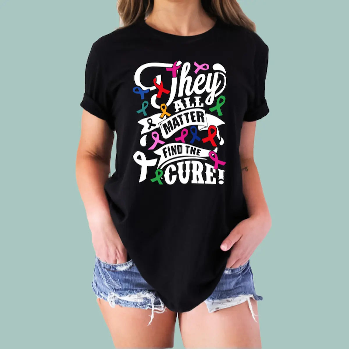 Woman wearing a black "They All Matter" cancer awareness tee with a colorful ribbon heart design.