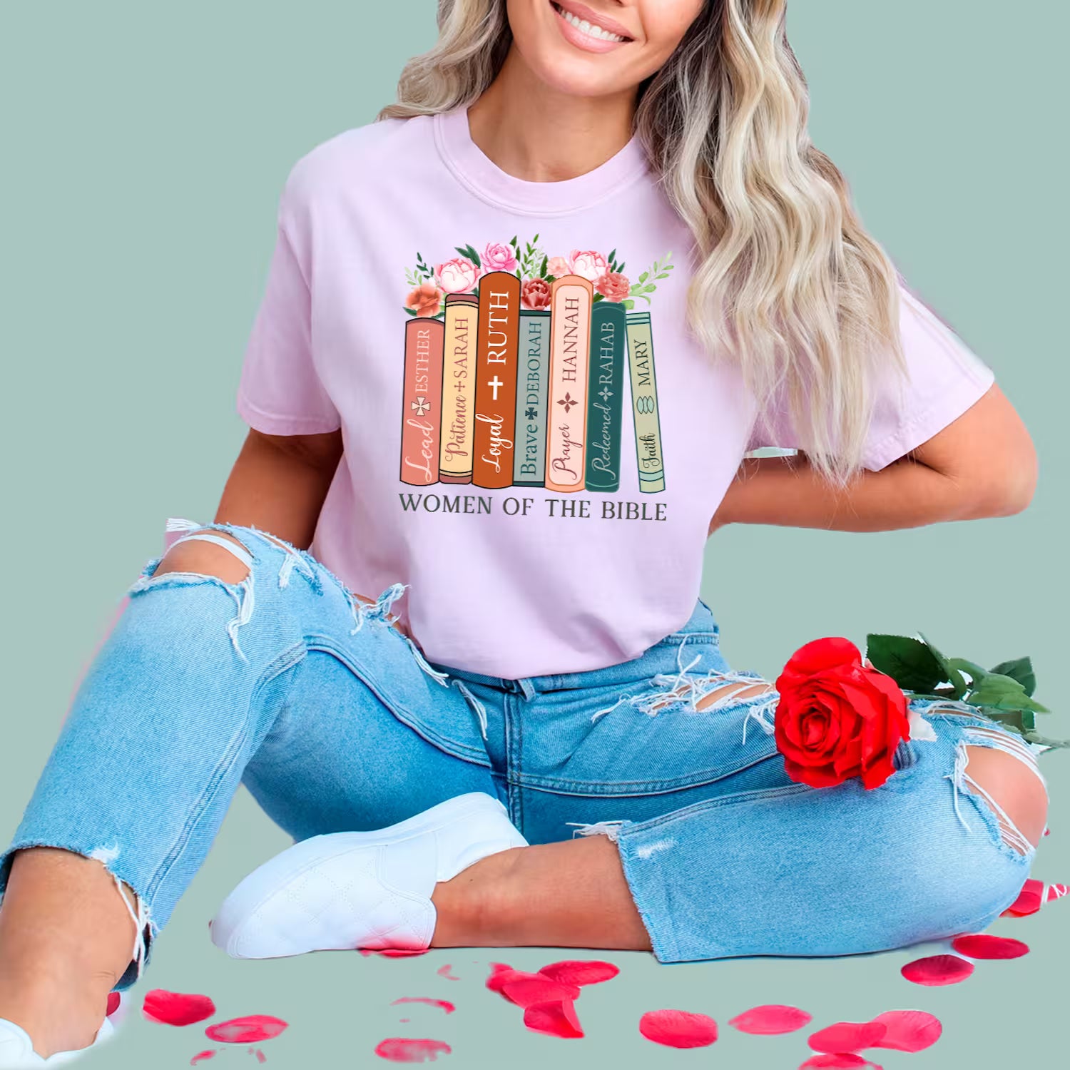 Woman wearing a pink Christian t-shirt featuring a stack of books with names like Esther, Ruth, and Mary.